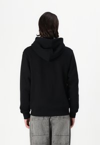 Schwarzer Kapuzenpullover mit lässiger Passform, aus strukturiertem Stoff und mit gerippten Bündchen. Kombiniert mit grauen gestreiften Cargo-Hosen.
