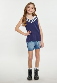 Marineblå ærmeløs top med hvid V-hals og detaljer med tre striber, parret med denimshorts og sorte snørebåndsstøvler, hvide ribbede sokker.
