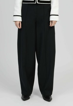 Pantalon noir à jambes larges porté avec une veste blanche ornée de bordures noires aux manches et à l'ourlet, assorti de chaussures noires à bout pointu.