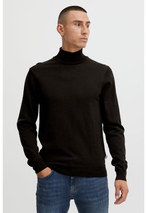 Zwarte coltrui van fijne gebreide stof, met lange mouwen en een aansluitende pasvorm, gecombineerd met blauwe jeans.