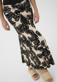 bézs színű maxi szoknya, nagy fekete levélmintákkal. Simák textúra, enyhén harang alakú dizájn, fonott platform szandálokkal párosítva.
