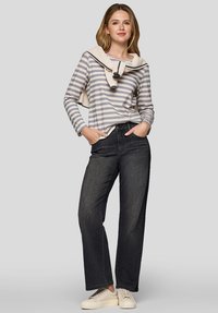 Gestreiftes Langarmoberteil mit einem cremefarbenen Kragen, kombiniert mit hochgeschnittenen dunkelblauen Jeans und hellen Sneakers. Einfarbige Farben, lässige Passform.