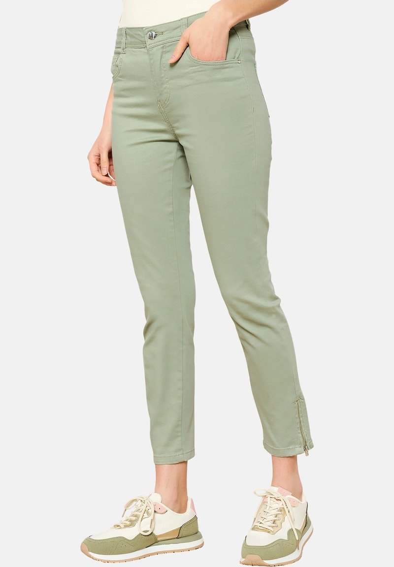 Lichtgroene slim-fit broeken van rekbaar materiaal met zijritsen bij de manchetten, gecombineerd met beige en groene sport sneakers.