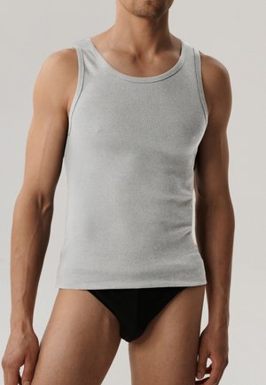 Męski tułów ubrany w dopasowany jasnoszary tank top i czarne majtki na prostym, jasnym tle.