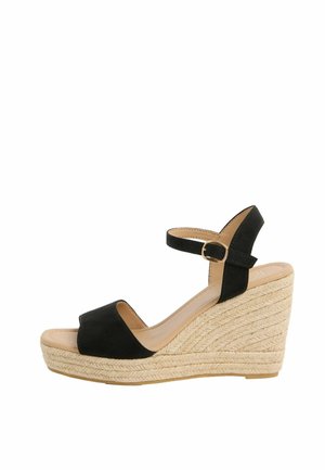 Černá otevřená kotníková klínová sandál s proplétanou platformou z juty a páskem kolem kotníku s malou zlatou přezkou.