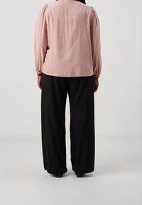 Blusa rosa a maniche lunghe con spalle arricciate, abbinata a pantaloni neri dalla vestibilità ampia. Tessuto morbido, design semplice e minimalismo nei dettagli.