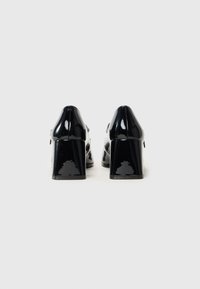 Black patent leather high-heeled shoes with a chunky block heel. Smooth texture, pointed toe, and minimal stitching detail on the back.