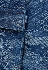 Tissu en denim bleu foncé avec un motif déchiré. Comprend une couture d'épaule, un rabat replié et une étiquette bleue avec le texte "MUSTANG".