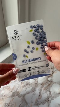 Ansiktsmaskeemballasje merket "Blåbær," med en hvit bakgrunn med blå blåbær og grønne blader. Inkluderer ikoner for vegansk og klimakontribusjon.