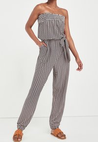 Sort og hvid mønstret jumpsuit med en smocket båndløse top, indsnævret talje, sidelommer og tapered ben. Kombineret med brune sandaler.