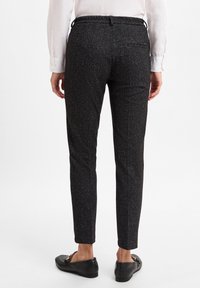 Schlanke Passform-Hosen im schwarz-grauen Fischgrätmuster. Der Stoff hat eine feine Textur, mit einem Bund und einer einzelnen Gesäßtasche.