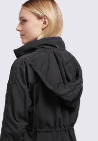Black lightweight jacket with a high collar and adjustable drawstring waist. Features a detachable hood and zippered side pockets.
