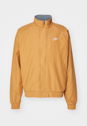 Giacca in nylon arancione con colletto alto, polsini e orlo elasticizzati. Presenta un logo Nike bianco sul lato sinistro del petto e due tasche laterali.