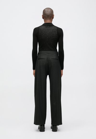 Crna majica dugih rukava s teksturiranim stražnjim dijelom, uparena s hlačama širokog kroja s uzorkom pinstripe i visokim strukom. Glatka tkanina i kroj koji se dobro uklapa.