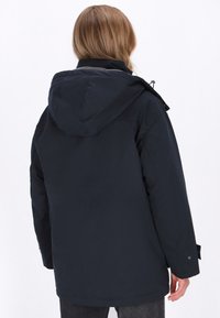 Mørkeblå vandtæt parka med hætte, der har en glat tekstur, justerbare snore og sidelommer. Bagsiden viser ingen synlige logoer.