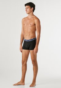 Schwarze Boxershorts mit einem marineblauen elastischen Bund, der weißen Logotext aufweist. Figurbetonter Schnitt, glattes Material, ohne sichtbare Muster.
