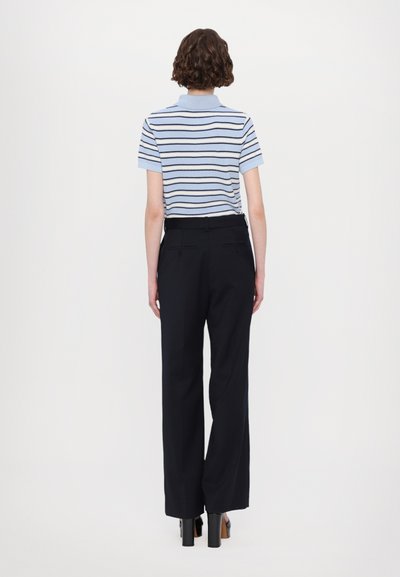 Gestreiftes Strick-Polohemd in Hellblau und Marineblau, kombiniert mit hochtaillierten schwarzen weiten Hosen. Das Model steht von hinten und zeigt die Details.