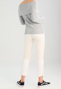 Pull gris clair côtelé à épaules dénudées, jean blanc court avec ourlet effiloché, et baskets noires. Design simple et coupe décontractée.