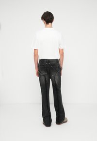 Jeans de ganga pretos com um corte relaxado, apresentando detalhes desgastados na parte de trás, e uma t-shirt branca simples. O fundo é branco liso.