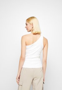 One-shoulder white tank top made of stretchy cotton. Fitted design with a smooth texture, worn with light beige cargo pants.