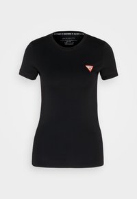 Musta hyvin istuva lyhythihainen t-paita, jossa on pieni punainen ja valkoinen kolmionmuotoinen Guess-logo vasemmassa rinnassa.