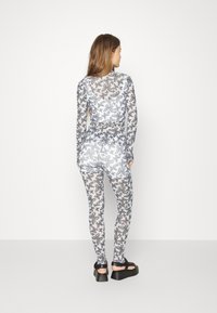 Bodysuit de mangas compridas feito de um tecido leve, com um padrão de borboletas em preto e branco, design ajustado e decote arredondado.