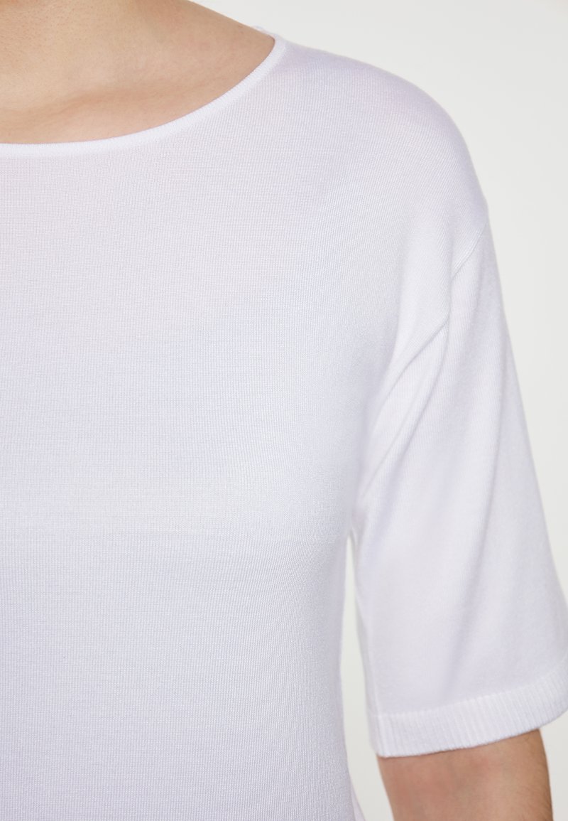 Witte gebreide top met een ronde halslijn en korte mouwen, met een gladde, lichte textuur en ribbelaccenten op de mouwen.