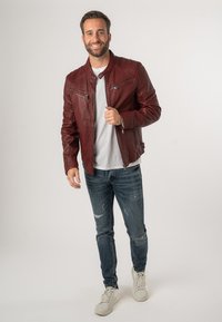 Burgunderfarbene Lederjacke mit Reißverschluss, zwei vorderen Taschen und einem schlanken Design, kombiniert mit abgenutzten blauen Jeans und weißen Sneakers.