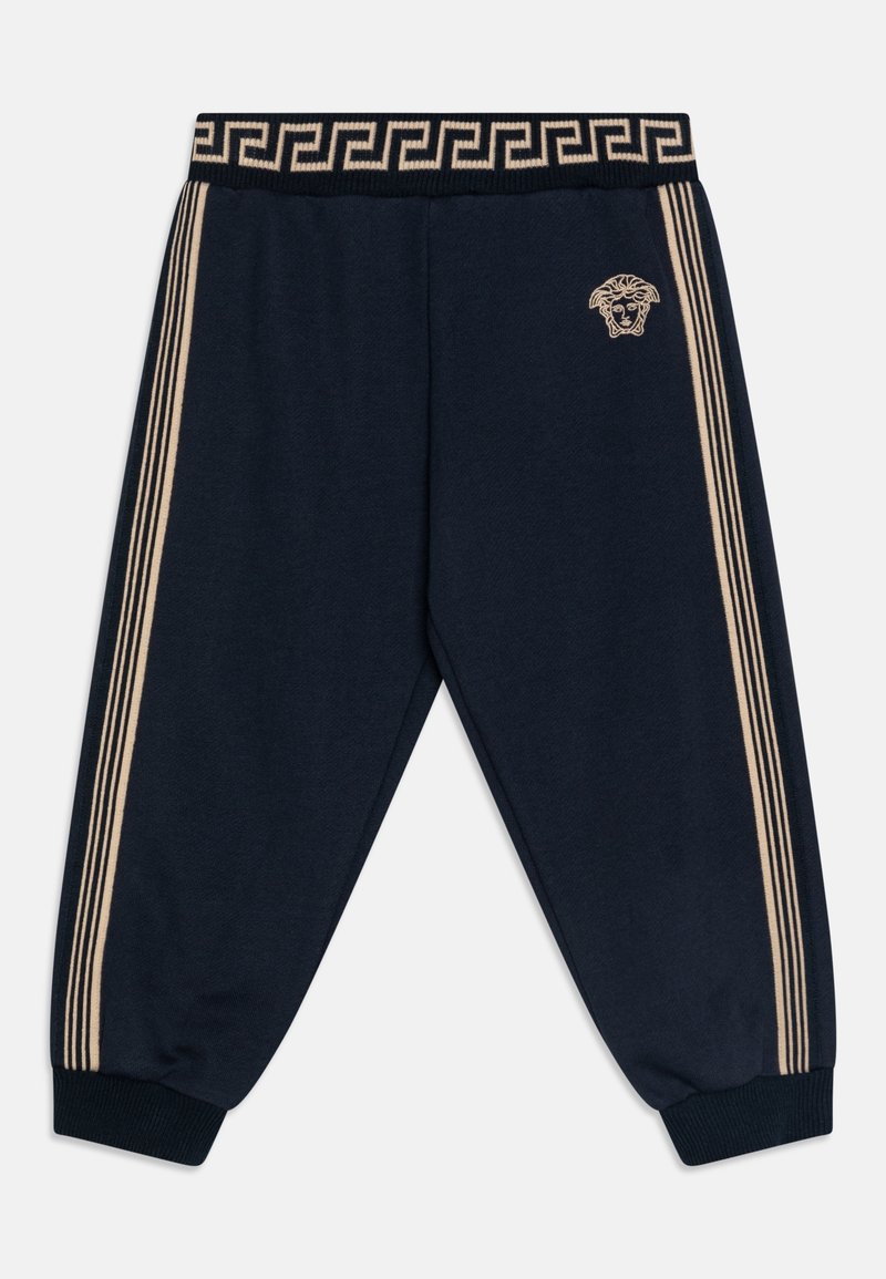 Pantalon de survêtement bleu marine avec bandes latérales beige, bords côtes aux poignets et à la taille arborant un motif clé grecque et un petit logo tête de Méduse.
