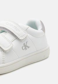 Baskets en cuir blanc avec une bande velcro et un détail en logo argenté. Doublure intérieure texturée et semelle en caoutchouc pour une meilleure adhérence.