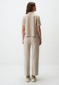 Top a maniche corte in maglia beige con colletto alla coreana abbinato a pantaloni a gamba larga dello stesso colore. Texture morbida e design casual.