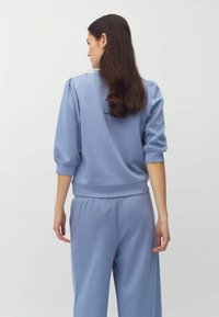 Felpa azzurro chiaro con maniche a sbuffo e polsini elastici, abbinata a pantaloni larghi coordinati. Tessuto morbido, stile casual.