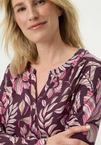 Lila Bluse mit floralem Muster in Rosa, Beige und Creme. Verfügt über einen Rundhalsausschnitt und lange Ärmel, gefertigt aus einem weichen Stoff.