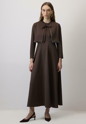 Pruun pikkade varrukatega kleit, millel on keha kohal istuv osa, laienev seelik ja lipsu detail. Kaunistatud valgete pärlitega lühikese jope hem. 