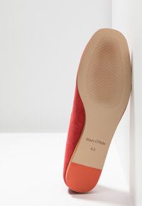 Chaussure en suède rouge avec une semelle solide couleur tan, présentant une texture lisse et un motif légèrement nervuré au fond. Le nom de la marque "Marc O'Polo" est visible.