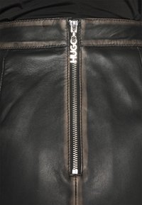 Zwart lederen kledingstuk met een verticale zilveren rits voorzien van een trekker gegraveerd met de merknaam "HUGO".