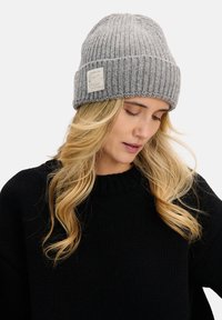 Szara prążkowana dzianinowa czapka z podwiniętym mankietem, z małą naszywką z logo. Miękka w dotyku i dopasowana, zaprojektowana, aby zapewnić ciepło w zimne dni.