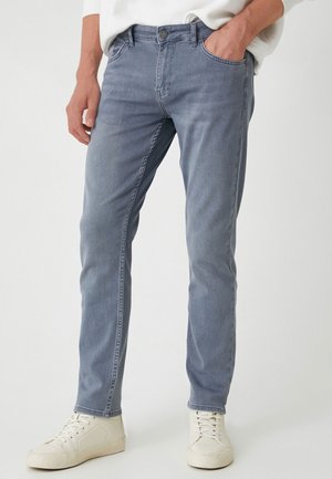 Light blue denim jeans with a slim fit, featuring a classic five-pocket design and a button closure. Worn with white sneakers.