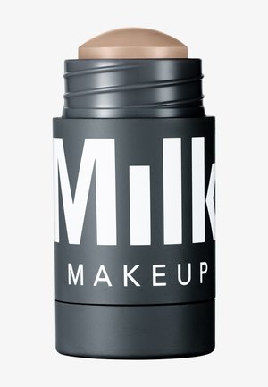 Black cylindrical container with large white text, topped with a beige, rounded stick. Smooth matte finish, compact size for makeup application.