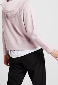 Sweat à capuche court rose en tissu doux, doté d'une capuche, de manches longues et d'un ourlet côtelé, associé à un pantalon noir ample.