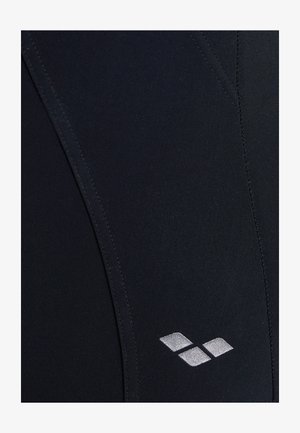 Schwarze sportliche Leggings aus glattem, dehnbarem Stoff. Verfügt über ein glänzendes silbernes Logo auf der unteren rechten Seite und flache Nähte.