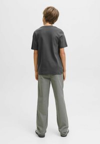 Child facing away, wearing a gray t-shirt and light green pants, standing against a minimalistic white background.