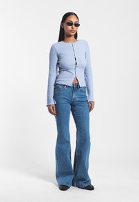 Light blue ribbed knit long-sleeve top with button closure, paired with flared dark blue denim jeans. Slim fit and textured fabric.