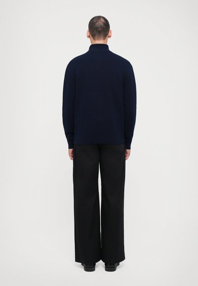 Suéter de punto azul marino con un cuello alto, combinado con pantalones negros de pierna ancha. Textura suave, diseño simple y sin patrones ni herrajes visibles.