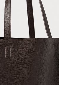 Dark brown textured leather tote bag with two straps and subtle embossed logo on the front.