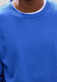 Sweat-shirt à col rond bleu avec une texture lisse. Présente un col côtelé et un tissu épais. Aucun logo ni motif visible.