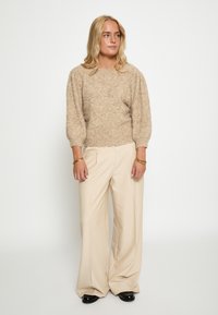 Bežani textured pulover s nabranim rukavima, uparen s laganim bež širokim hlačama i crnim cipelama. Jednostavan, meki dizajn tkanine.