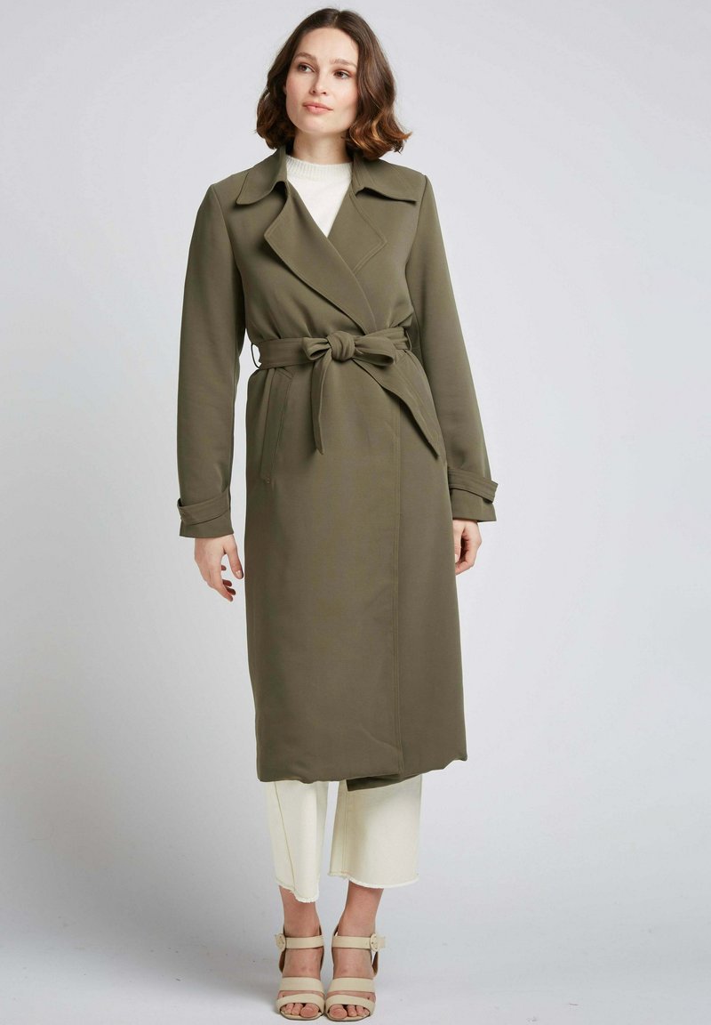 Manteau trench vert olive avec une taille à nouer, manches longues et larges revers, présentant une texture lisse et un design minimaliste.