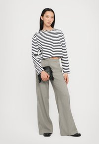 White and navy striped cropped sweater paired with gray pinstriped wide-leg trousers. Model holds a black fringed clutch. Flat shoes.