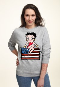 Sudadera gris que presenta un gráfico de una mujer de dibujos animados sentada sobre una bandera estadounidense. El diseño incluye colores rojo, azul y blanco con contornos negros.